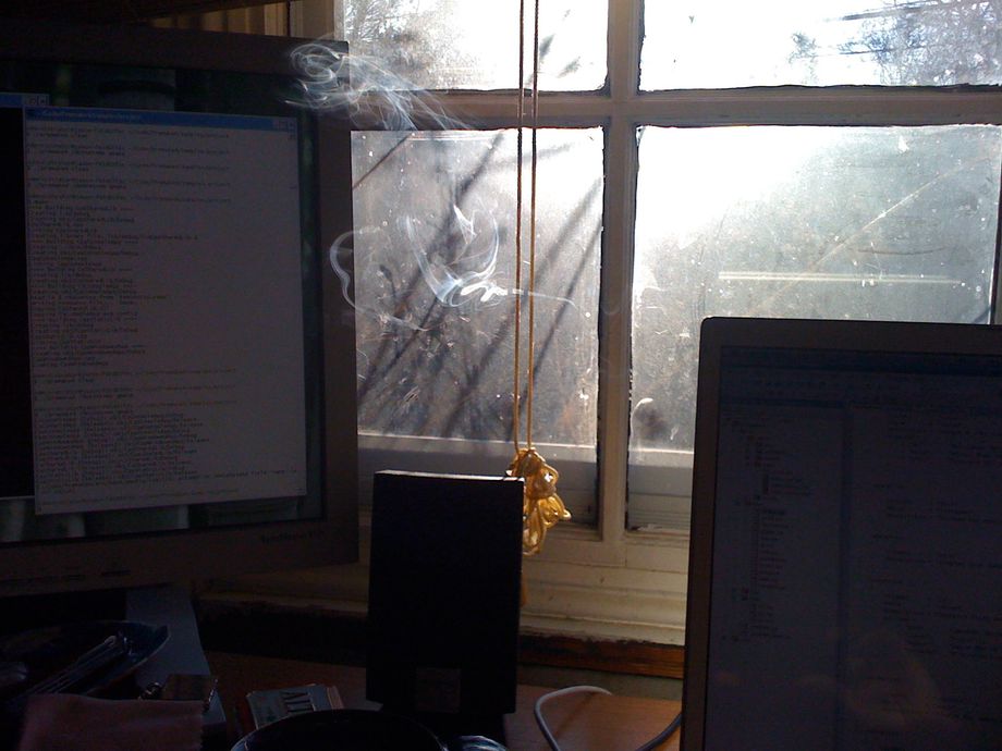 Incense smoke coils and drifts; dusty glass diffuses the sun in the window behind. 